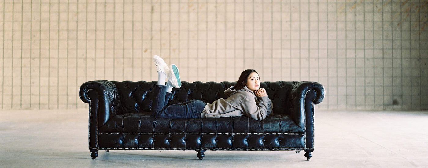 Model laying on a black leather couch wearing the White low top S1 Sneaker